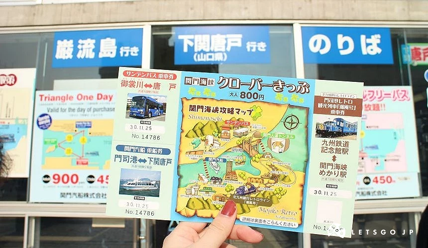 手持關門海峽四葉草車票,背景為售票窗口與交通資訊看板