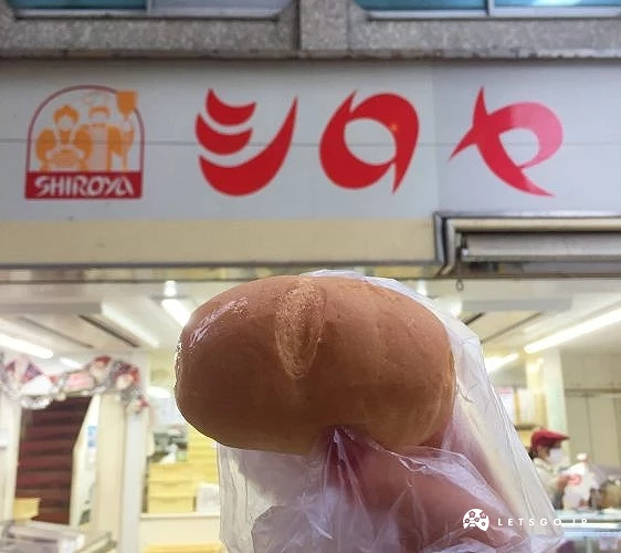 手持SHIROYA麵包,背景為店鋪招牌,為小倉知名平價甜點