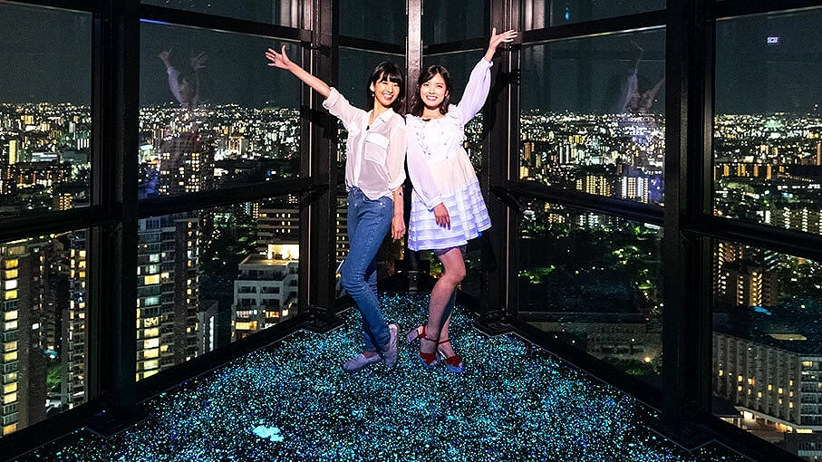 兩個女孩擺起姿勢拍照,後面是為美麗的高空夜景