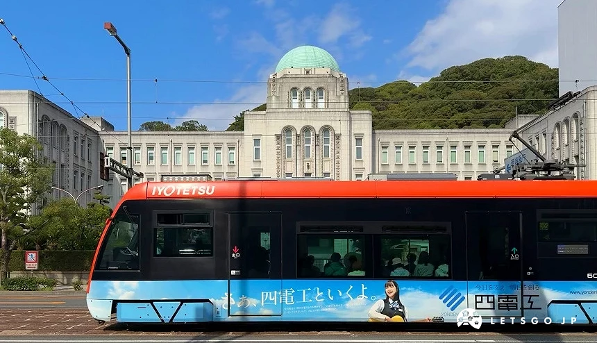 橘黑塗裝的伊予鐵道路面電車駛過松山市知名地標愛媛縣廳前方