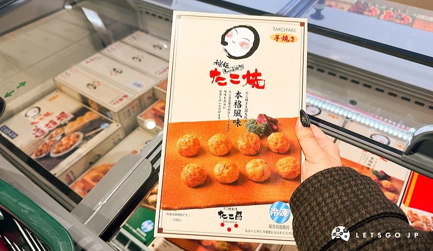 手持TAKO昌冷凍章魚燒盒裝商品,背景為陳列多款盒裝冷凍食品的商場冰櫃