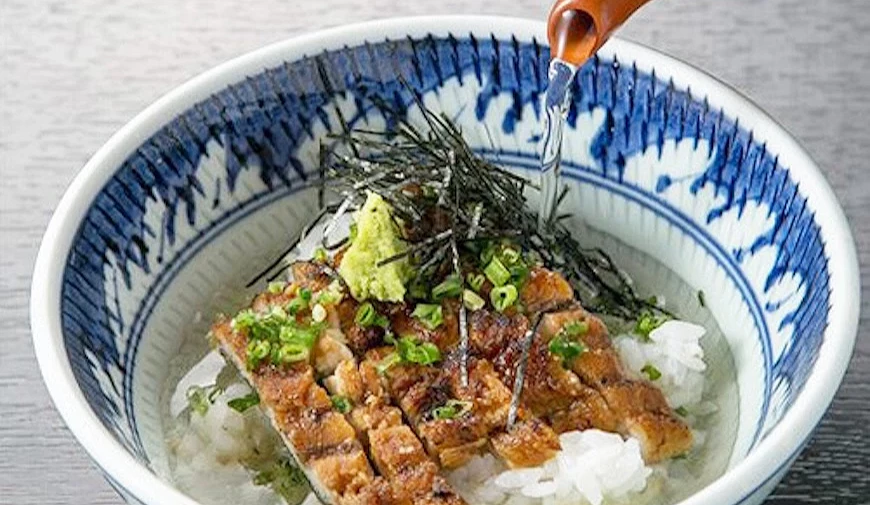 鰻魚飯碗上方淋入醬汁,搭配青蔥、山葵與海苔絲,盛裝於藍白花紋碗中