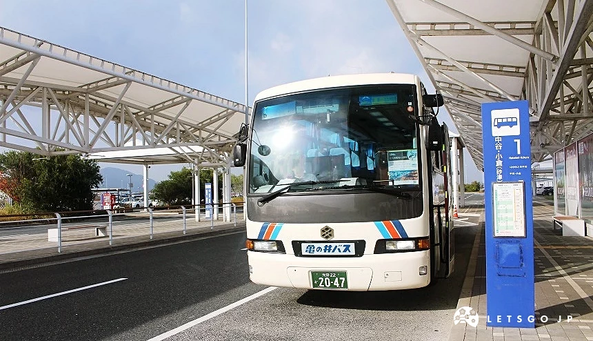 北九州機場外的巴士乘車處,一輛接駁巴士停靠在站牌旁,旁邊設有巴士時刻表看板與候車設施