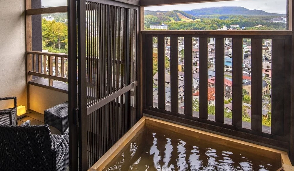 木質方型溫泉浴池,水流正注入池中,旁邊為設有戶外座椅的陽台空間