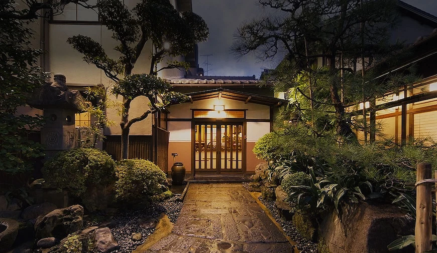 日式庭園入口夜景,石板小徑兩側種有松樹與灌木,木造玄關亮燈
