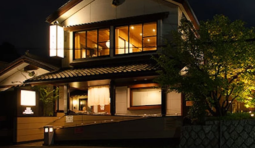 日式兩層建築餐廳外觀,夜間燈光照明,入口掛有白色暖簾