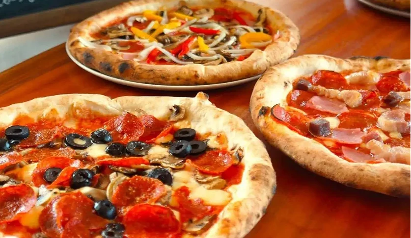 呈現「Pizzeria da ENZO」手工窯烤披薩的美食照片。木質餐桌上擺放著多款剛出爐、帶有焦香邊緣的拿坡里風披薩,包含舖滿薩拉米香腸與黑橄欖的經典口味,以及撒上鮮豔甜椒與洋蔥的蔬食款式。