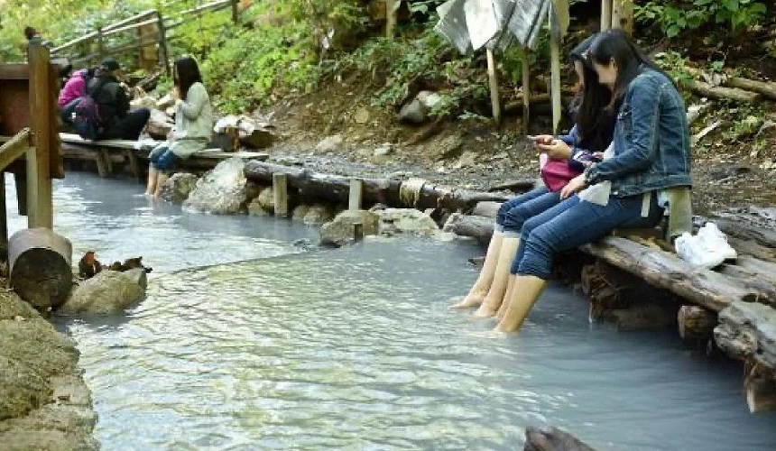 遊客們在河川旁享受天然足湯