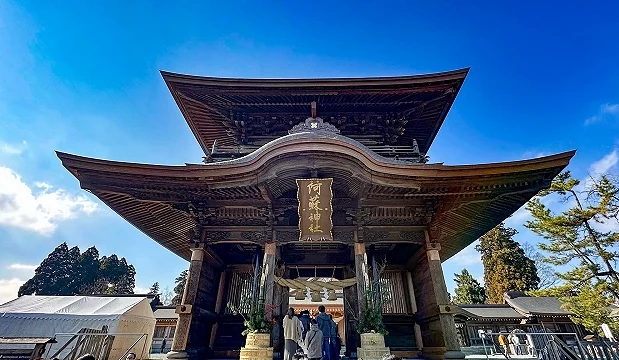 熊本縣阿蘇神社樓門正面,木造二層門樓前有參拜遊客,天空湛藍。
