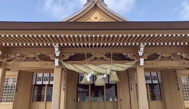 阿蘇神社拜殿正面近景,木造建築中央懸掛大型注連繩,前方設有賽錢箱