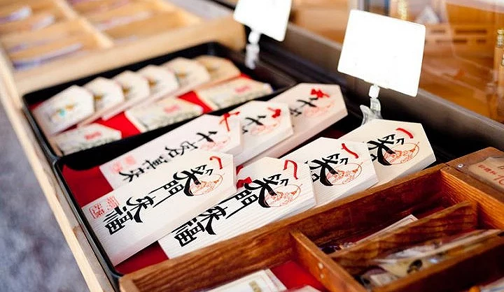 阿蘇神社授與所的御守與授與品陳列,木盒中擺放多款白色御守與祈願物