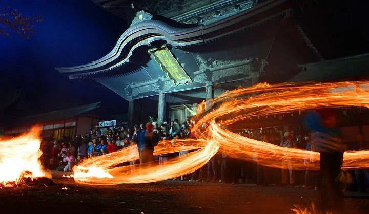 夜晚的阿蘇神社火振神事,參拜者在樓門前揮動燃燒火束,周圍聚集眾多觀眾