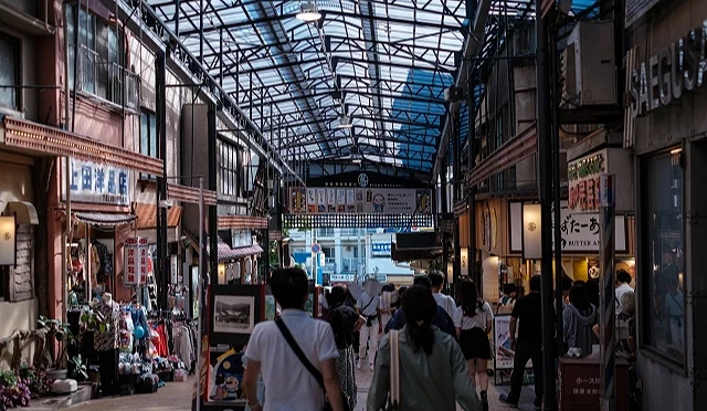 熱海站前商店街拱廊街景,兩側有餐飲店與伴手禮店,旅客在室內商店街散步