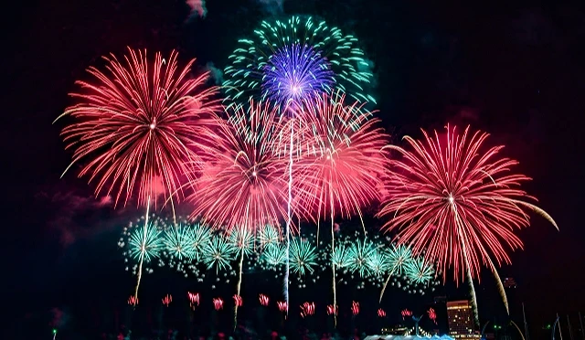 熱海海上花火大會夜晚煙火綻放,紅色、粉色與綠色大型煙火照亮海灣上空