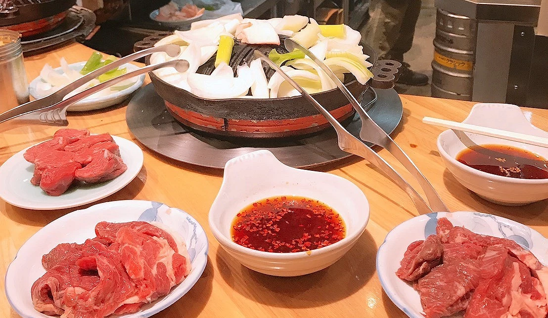 北海道成吉思汗烤肉用餐場景,鐵板上烤羊肉與洋蔥,搭配醬料與生肉盤