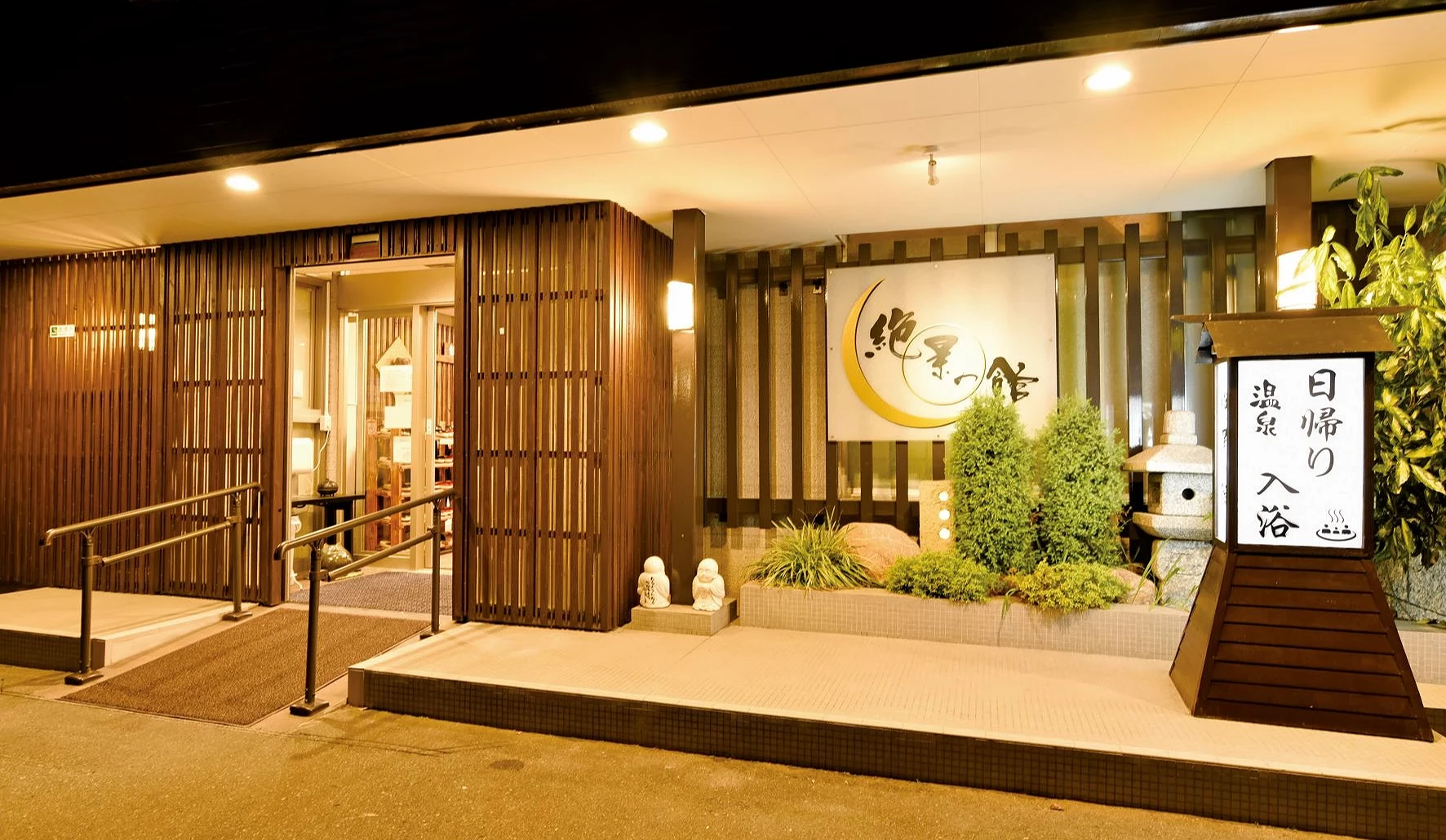 夜晚的絕景之館飯店入口亮著暖色燈光,門口可見「絕景之館」招牌與日歸溫泉入浴看板