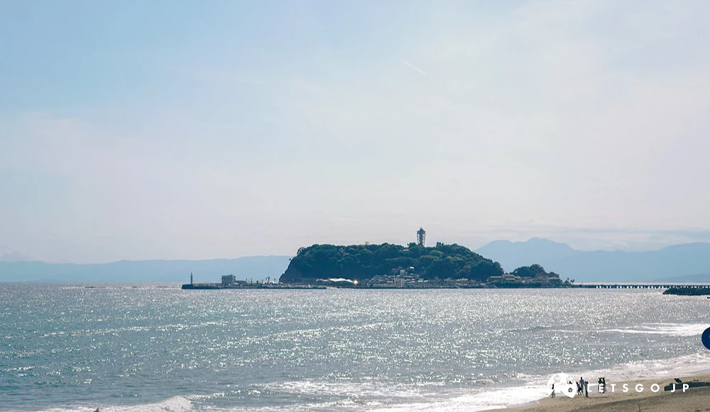 以日落餘暉與遠方山景剪影為背景的片瀨海岸,有幾個人在玩水上活動