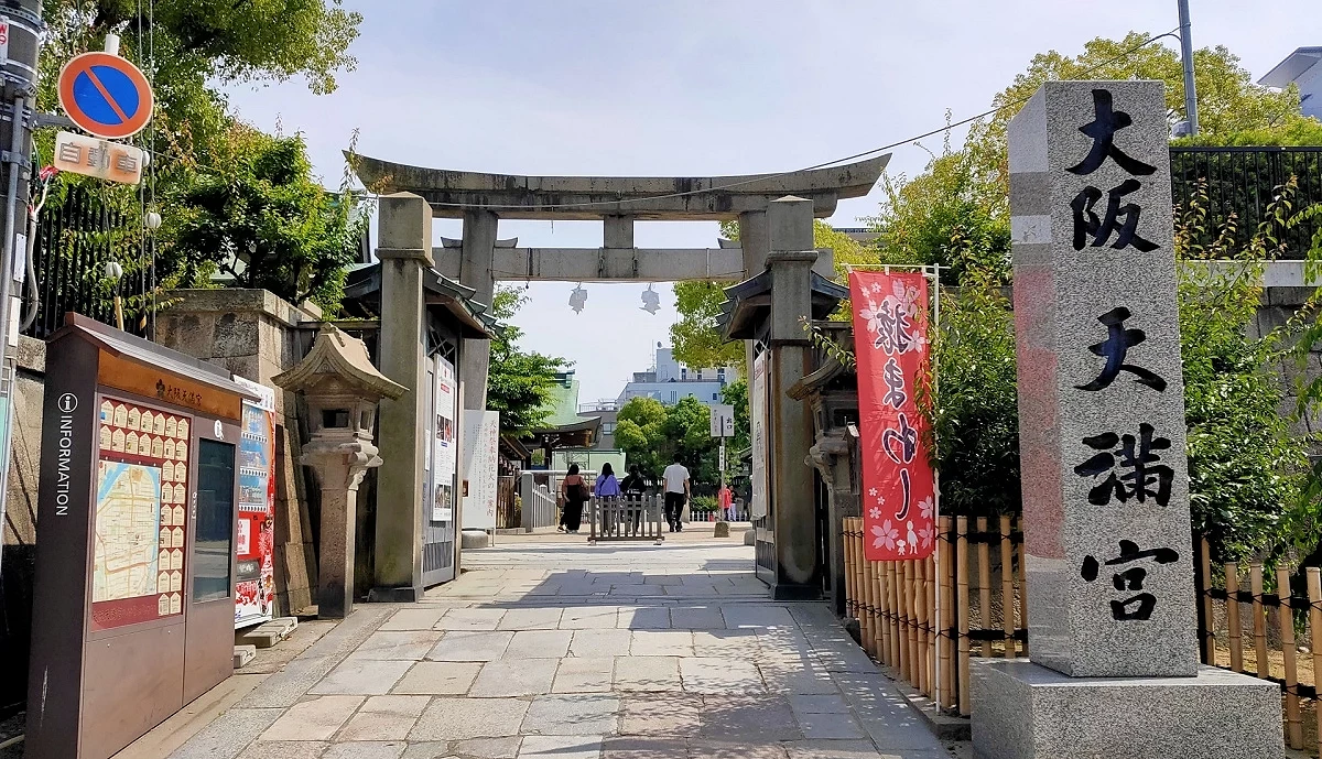大阪天滿宮石鳥居與入口步道,右側石碑寫有神社名稱,參拜者沿著石板路進入境內