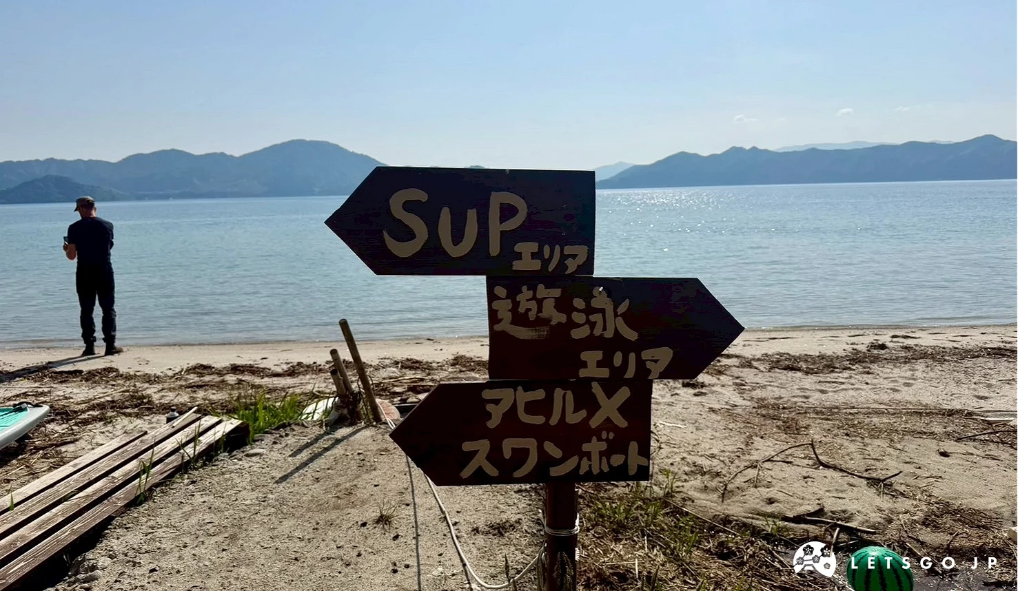 沙灘上立著一根深褐色木製指標,分別指向SUP區域與遊覽船乘船處。