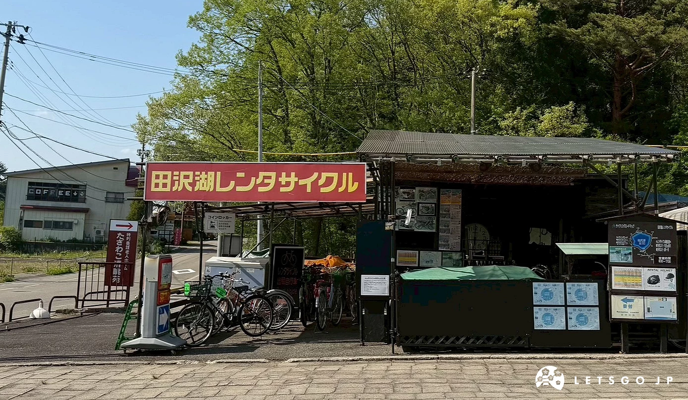 綠色樹林前設有一家掛著紅色招牌的田澤湖腳踏車出租店鋪。