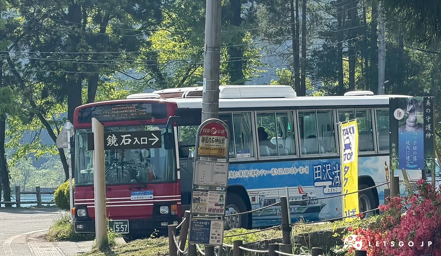 一輛紅白色相間的羽後交通路線公車,停靠在馬路旁的站牌前方。