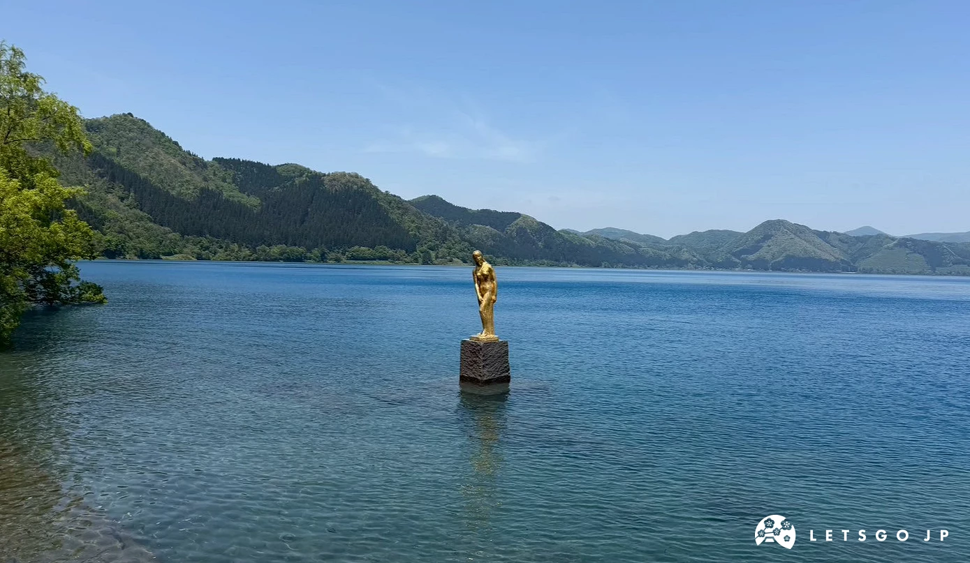 金色辰子雕像佇立在平靜清澈的藍色湖水中,遠方可見淡淡的山巒輪廓。