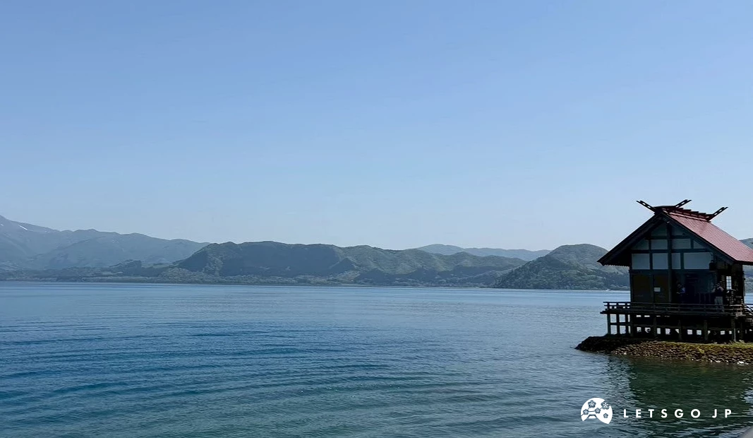 廣闊平靜的湛藍湖面延伸至遠方的綠色山巒,天空晴朗無雲。