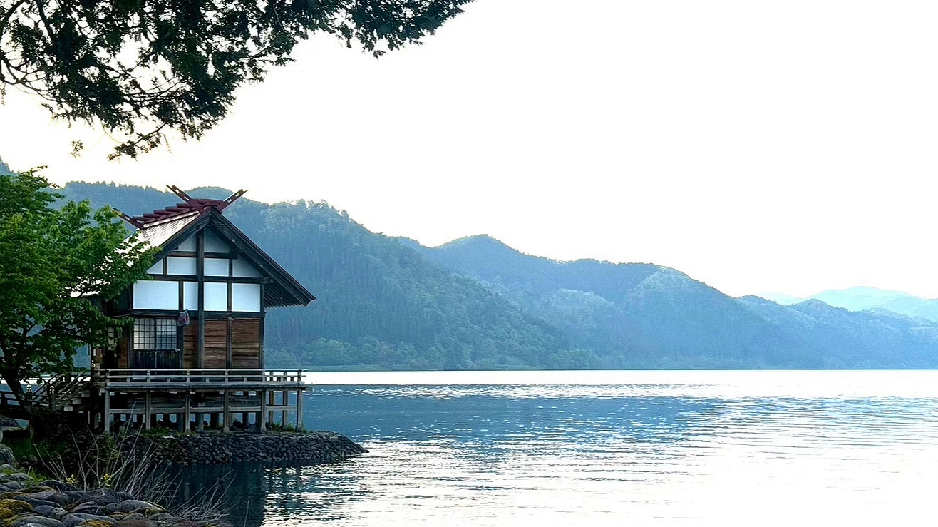 平靜的鈷藍色湖水旁,岸邊矗立著一座帶有黑色屋頂的古典木造建築。