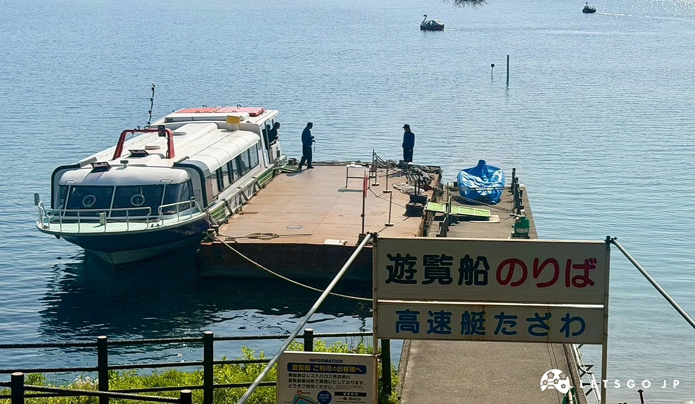 大型觀光遊覽船停靠在寫有遊覽船乘船處的木製棧橋旁,有船員在岸邊走動。