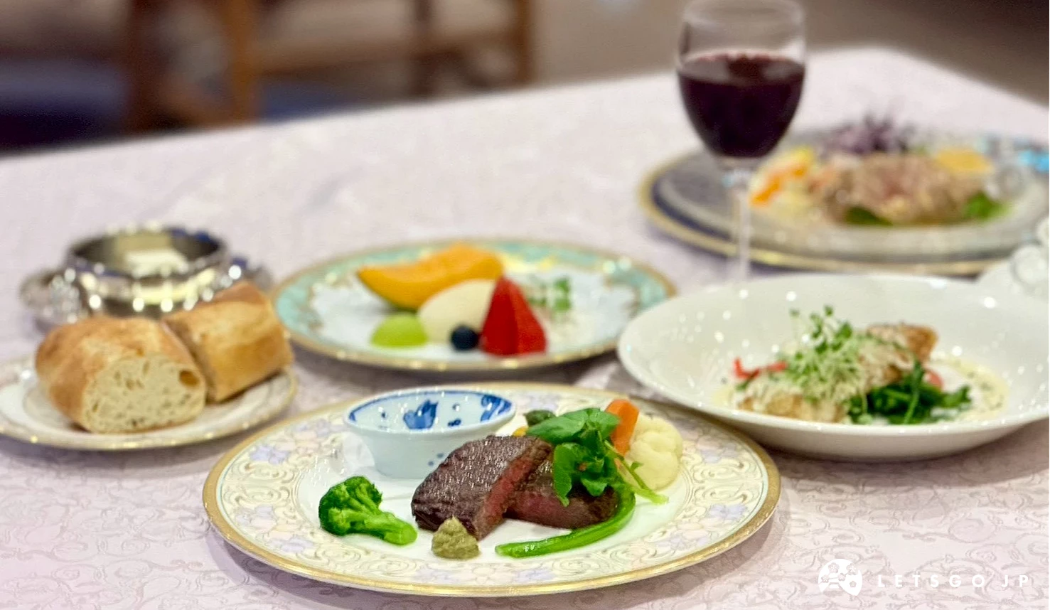 白色餐桌上擺放著精緻的法式牛肉主菜、麵包與紅酒。