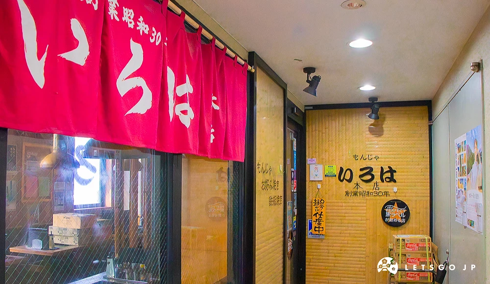 文字燒いろは本店入口 位於走廊盡頭的文字燒店,門口掛有紅色暖簾,黃色竹簾牆面寫著「いろは本店」。