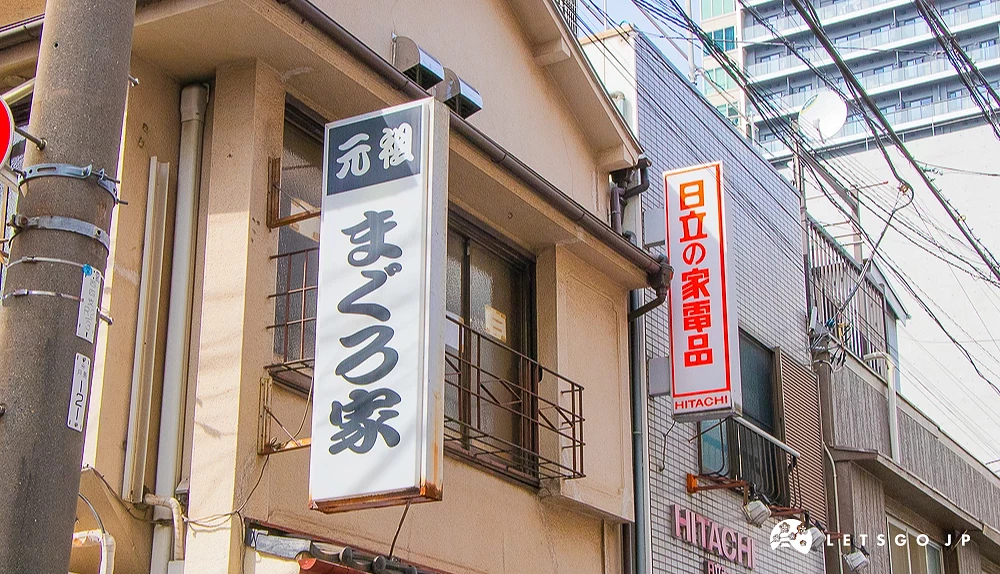 まぐろ家與日立電器招牌 住宅外牆掛有「元祖まぐろ家」直式招牌,後方緊鄰「日立の家電品」的紅白招牌。