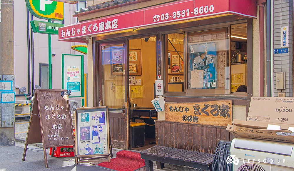 もんじゃまぐろ家本店 まぐろ家本店外觀,紅色遮雨棚印有電話,櫥窗內貼有棒球員海報,門口擺放菜單看板。