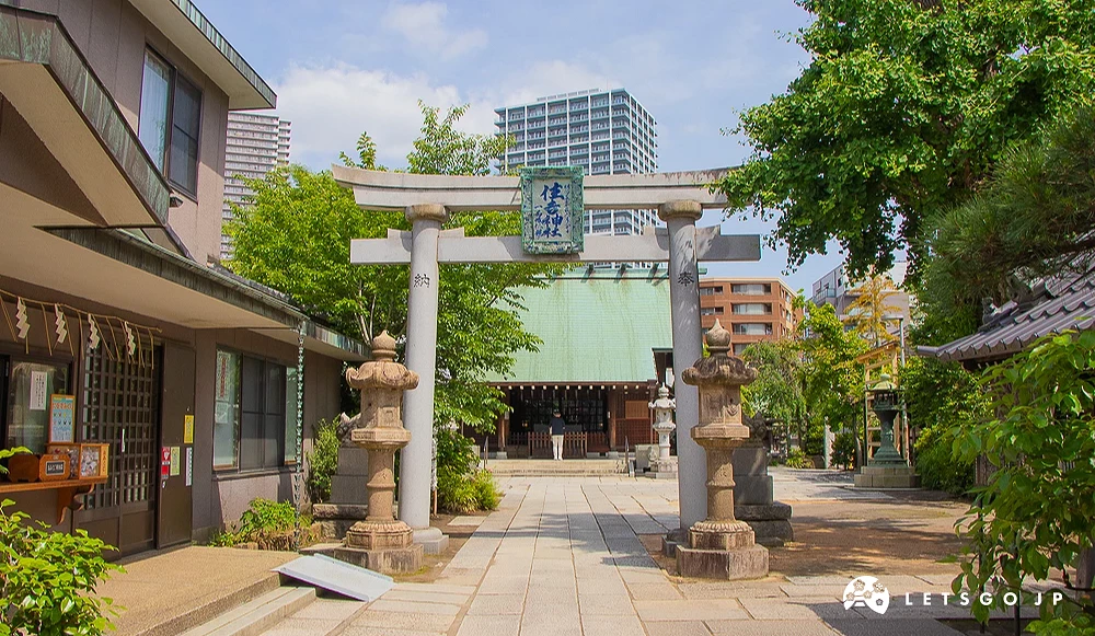 住吉神社鳥居與拜殿 住吉神社的石造鳥居立於參道前,上方有青銅匾額,遠處為拜殿與高層建築。