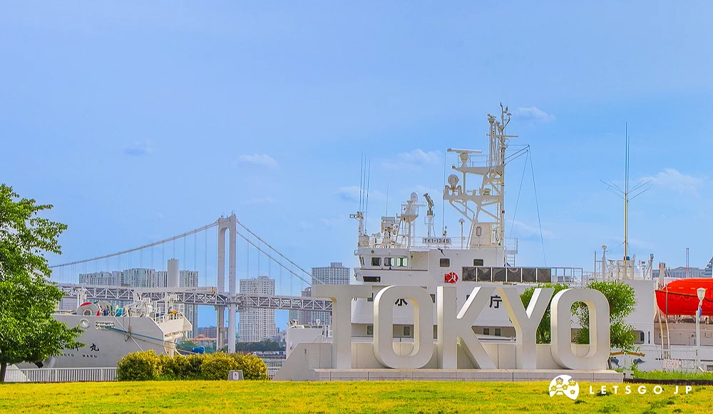 晴海客運碼頭與 TOKYO 標誌 綠色草坪上立有白色「TOKYO」大型立體字樣,背景為白色船隻與遠處的彩虹大橋。