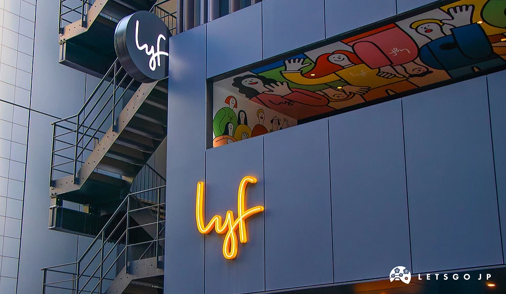 lyf 飯店外牆設計 現代化灰色建築外牆設有黃色「lyf」霓虹字樣,上方窗戶內有色彩鮮豔的卡通人物插畫。