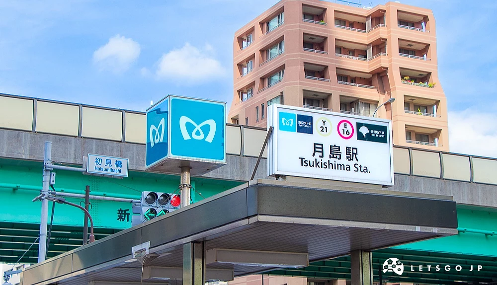 地鐵月島站出入口 東京地鐵與都營地下鐵的月島站出入口標誌,後方有綠色高架道路與住宅大樓。