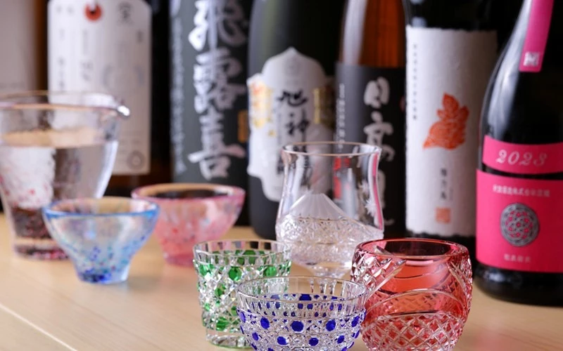 桌上排列多瓶日本清酒與彩色江戶切子酒杯,寫有日文標語