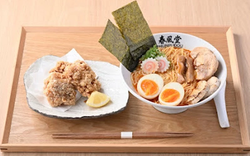 木托盤上放春風堂拉麵碗與炸雞塊,拉麵附海苔、溏心蛋與叉燒