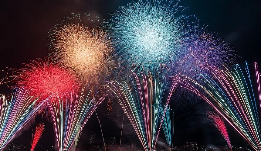 江戶川區花火大會夜空中綻放紅色、金色、藍色與粉色大型煙火,下方有多道彩色光束向上升起