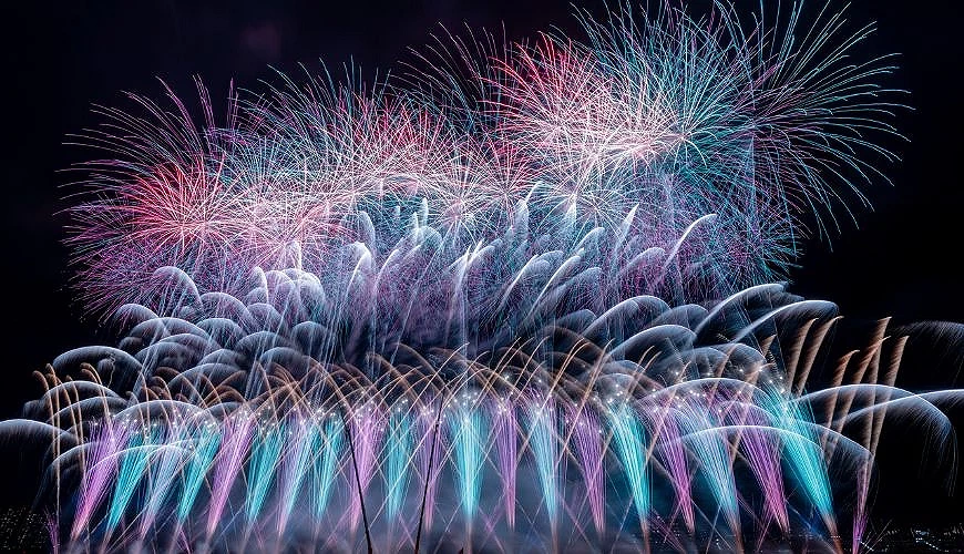 江戶川區花火大會夜空中施放大量藍綠色、粉紅色與白色煙火,形成層次豐富的連發畫面
