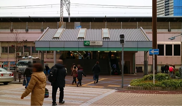 JR 小岩站出入口前有行人通過,車站上方可見鐵道路線與站名標示