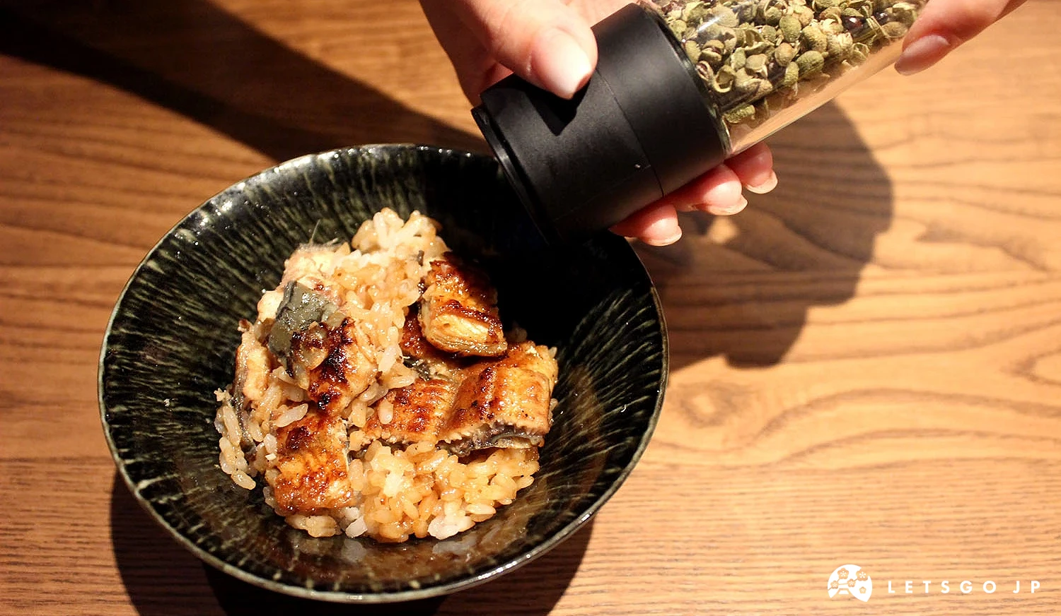 手持山椒罐,將山椒加入鰻魚飯中。