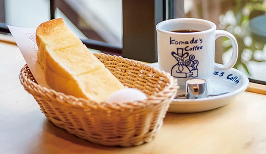 Komeda's Coffee 品牌馬克杯與厚片吐司置於藤籃中,擺放在木桌靠窗位置