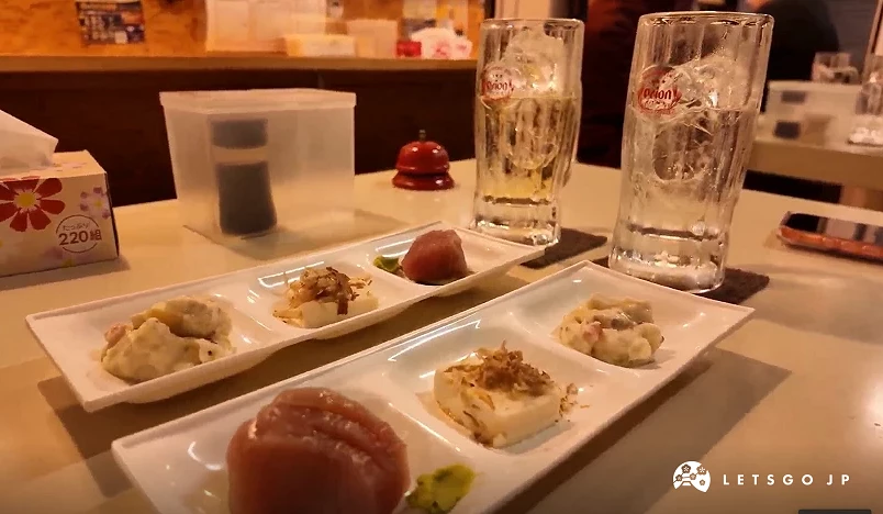 桌上有兩杯酒杯,前面有各三格的小菜碟,小菜碟上有鮪魚生魚片,豆腐
