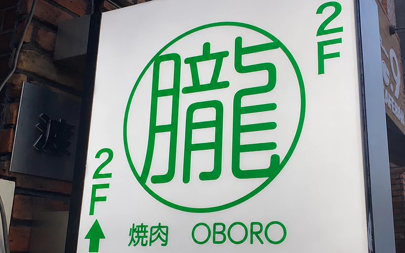 戶外招牌寫有「朧」「焼肉 OBORO」「2F」，白底綠字，附向上箭頭