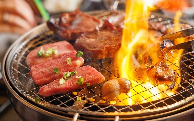 炭火烤爐上同時燒烤多塊牛肉，部分撒有蔥花，火焰旺盛