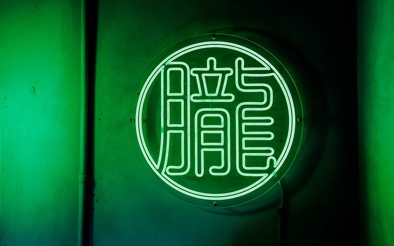 綠色霓虹燈圓形招牌，中央漢字「朧」發光於暗色背景