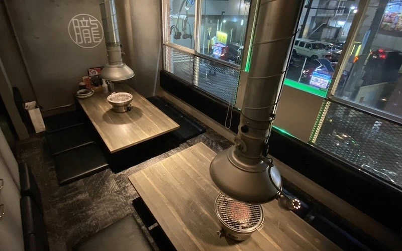 燒肉店挖坑式座位區，每桌設有炭火烤爐與排煙罩，牆上印有「朧」字