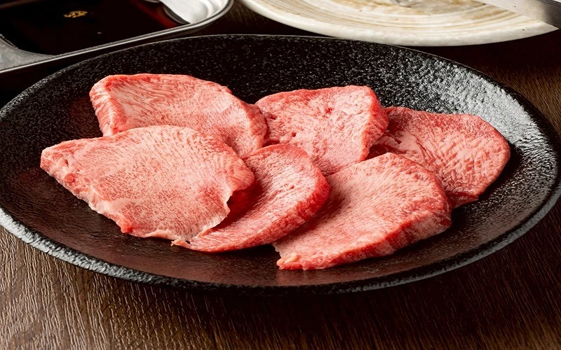 五片薄切牛舌盛於黑色橢圓盤,肉質紋理清晰